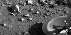 This is the first photograph ever taken on the surface of the planet Mars. It was obtained by Viking 1 just minutes after the spacecraft landed successfully early today [July 20, 1976]. We see both rocks and finely granulated material--sand or dust. Many of the small foreground rocks are flat with angular facets. Several larger rocks exhibit irregular surfaces with pits and the large rock at top left shows intersecting linear cracks. Extending from that rock toward the camera is a vertical linear dark band which may be due to a one-minute partial obscuration of the landscape due to clouds or dust intervening between the sun and the surface.